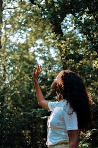 Rear view of woman with an arm outstretched standing against trees