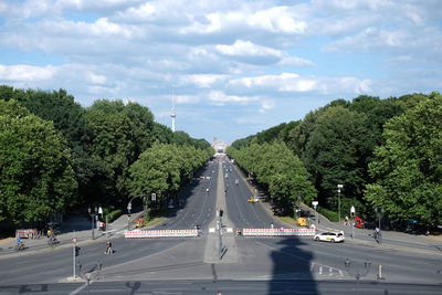 City street amidst trees against cloudy sky