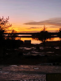 Silhouette trees by lake against sky during sunset