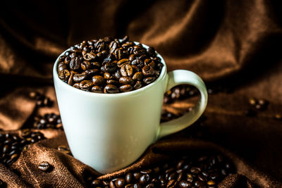 Close-up of roasted coffee beans with cup on fabric