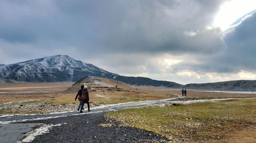 Rear view of hikers walking on footpath against mountains during storm clouds
