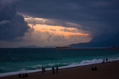 People at beach against sky during sunset