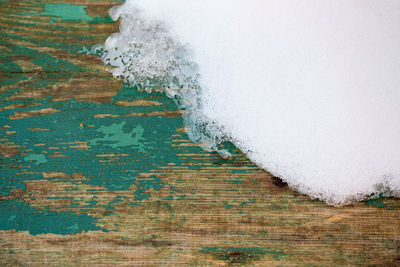 Old wooden plank background with snow and peeling green paint with selective focus.