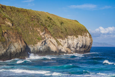 Scenic view of sea by mountain against sky