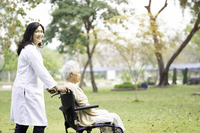 Portrait of nurse pushing senior woman sitting on wheelchair in park