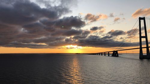 Silhouette bridge over sea against sky during sunset