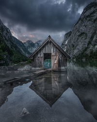Hut by lake and mountain against sky