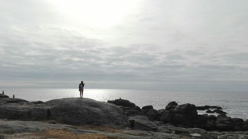 Rear view of man standing on rock by sea against sky