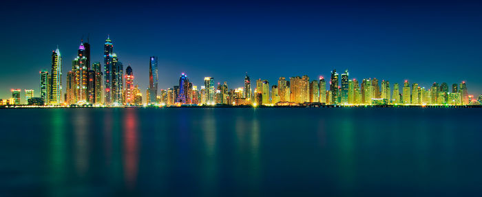 Panoramic view of illuminated buildings and sea against clear sky at night