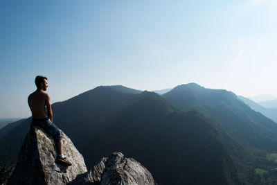 Rear view of man standing on mountain against blue sky