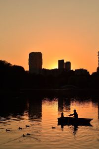 Silhouette birds on lake against orange sky