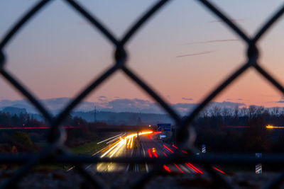Blurred motion of train in city seen through chainlink fence