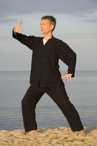 Man practicing tai chi at beach against sky