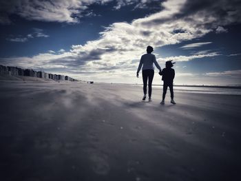 Silhouette friends standing on beach against sky