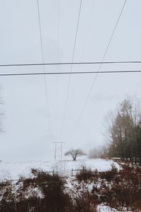 Electricity pylon on snow covered field against sky
