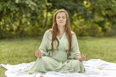 White pretty pregnant woman meditates in park, sits on blanket, stress relief,mindfulness. enjoying