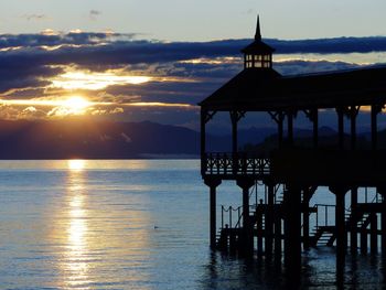 Silhouette gazebo by sea against sky during sunset