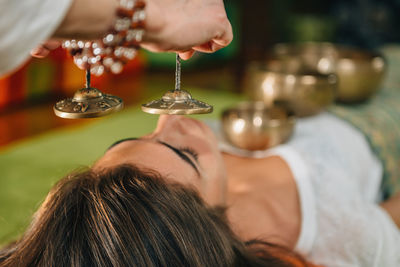 Cropped hand of therapist holding bell by young woman at spa