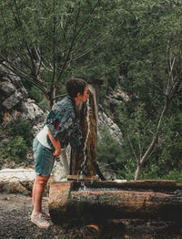 Elderly woman by the spring in the nature. senior woman drinking water from spring in the woods.