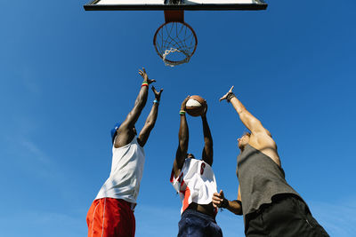 Low angle view of basketball hoop and men against blue sky