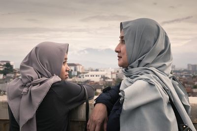 Close-up of mother and daughter standing in city against sky