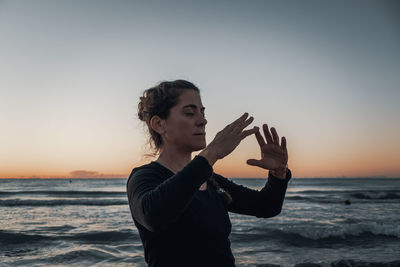 Woman standing at beach against sky during sunrise