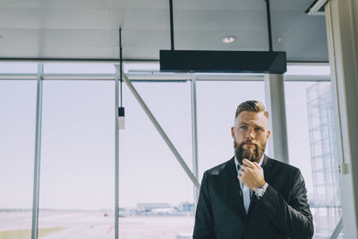 Thoughtful businessman standing against window at airport