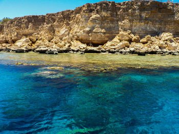 Scenic view of rocks by sea against blue sky