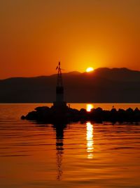 Silhouette cross on sea against orange sky