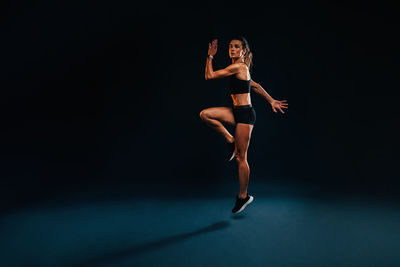 Full length of young woman exercising against black background