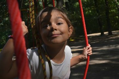 Portrait of girl making face while holding rope in forest