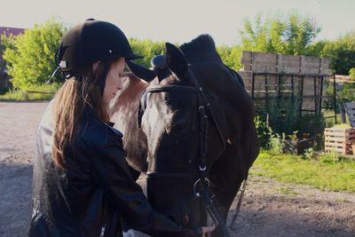 Rear view of women jockey feeding black horse at the ranch 