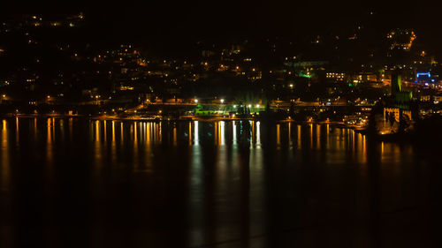 Illuminated buildings by river against sky at night