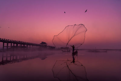 Silhouette man throwing fishing net over sea during sunset