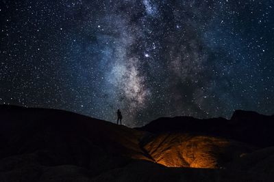 Silhouette person standing on landscape against star field at night