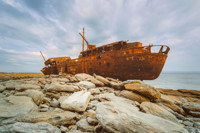 Shipwreck on rocks at beach against sky