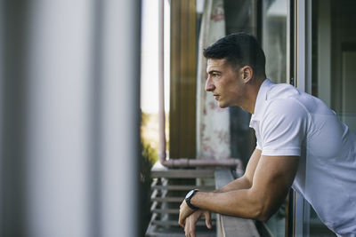 Side view of young man looking through window