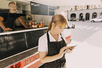 Female chef using mobile phone by food truck at city street