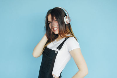 Portrait of young woman listening to music against blue background