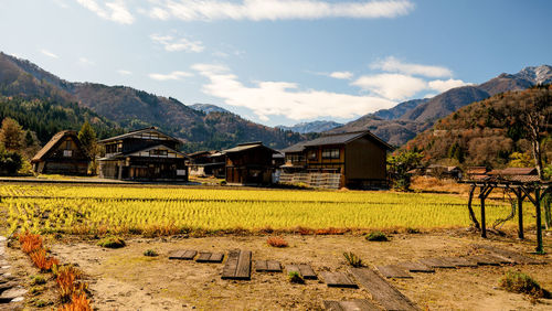 House on field by houses against sky