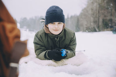 Portrait of smiling boy in knit lying on snow