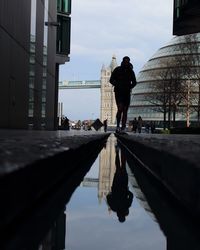Man walking on canal in city against sky
