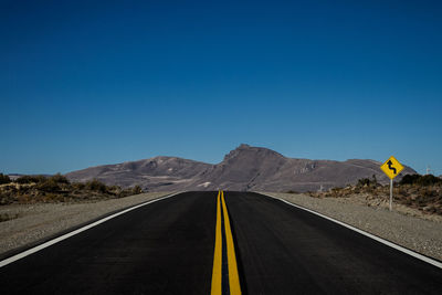 Road leading towards mountains against clear blue sky