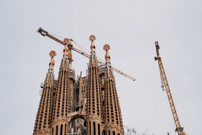 Low angle view of crane by building against sky