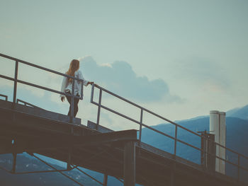 Low angle view of woman standing on railing against sky