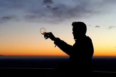 Silhouette man holding camera against sky during sunset