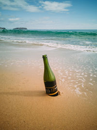 Green bottle on beach against sky