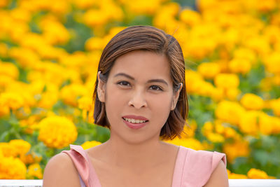 Portrait of smiling woman sitting against yellow flowers