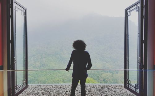 Rear view of woman looking at mountain through window 