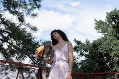 Low angle view of woman standing by trees against sky